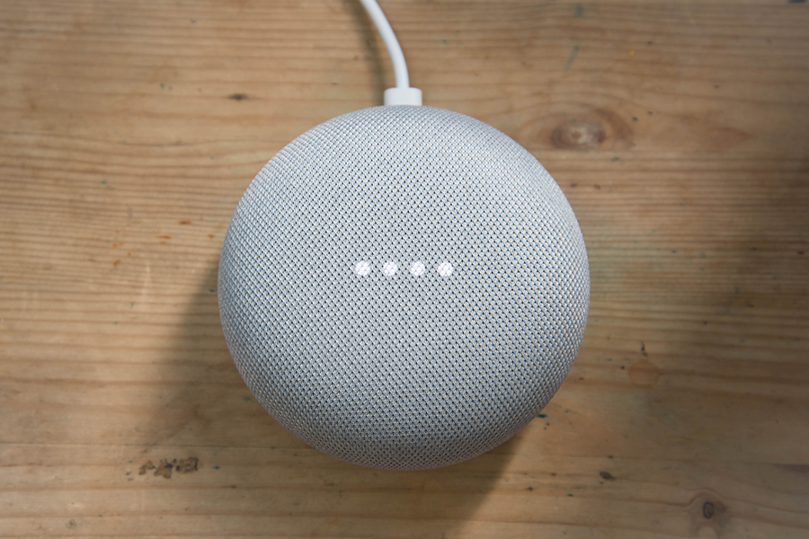A top-down photo of a smart speaker home assistant on a light wood background