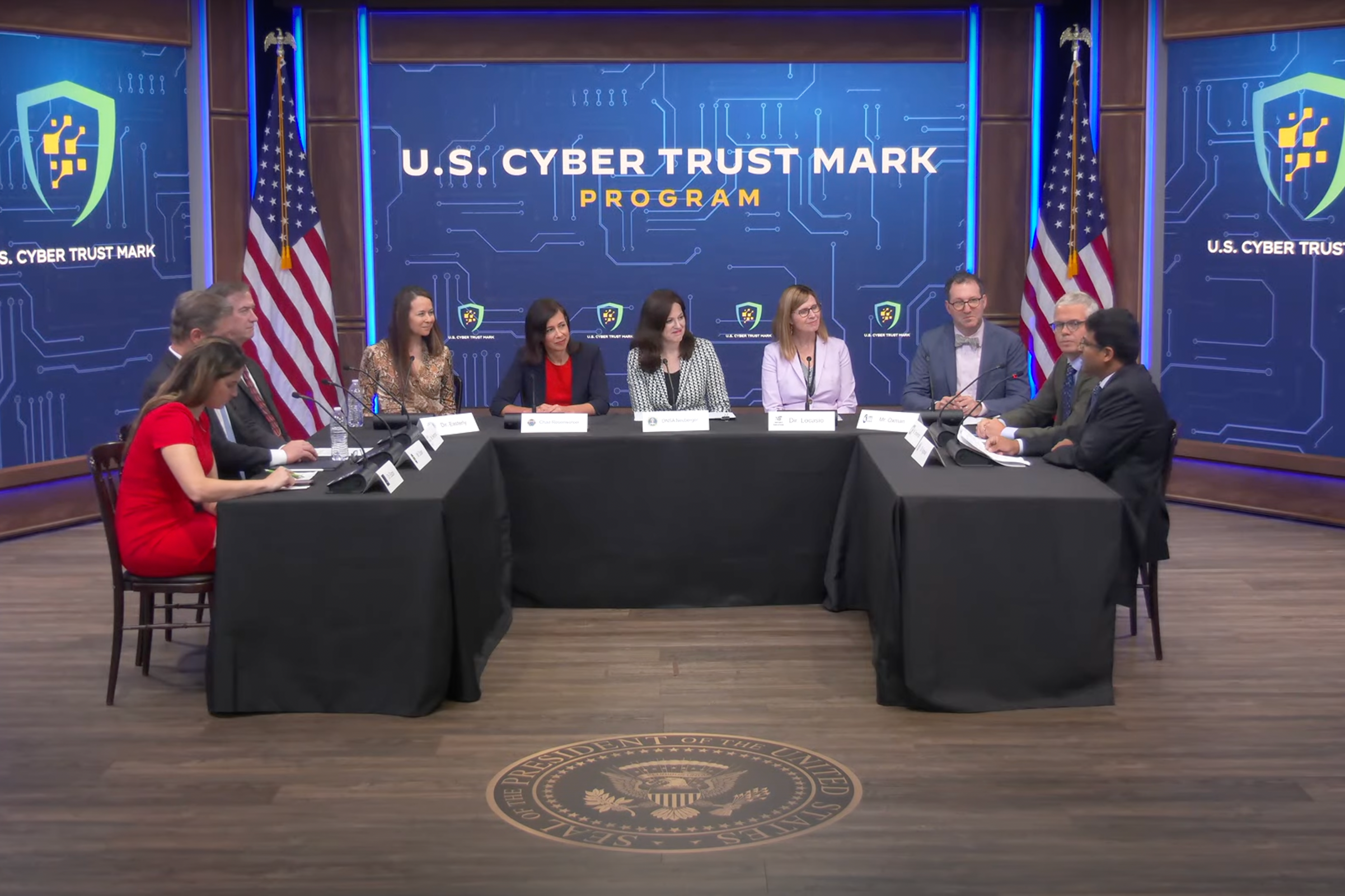 Stillframe of the livestreamed event showing a dozen or so people gathered around a semi circular conference table, the signage in the background reads "US Cyber Trust Mark"
