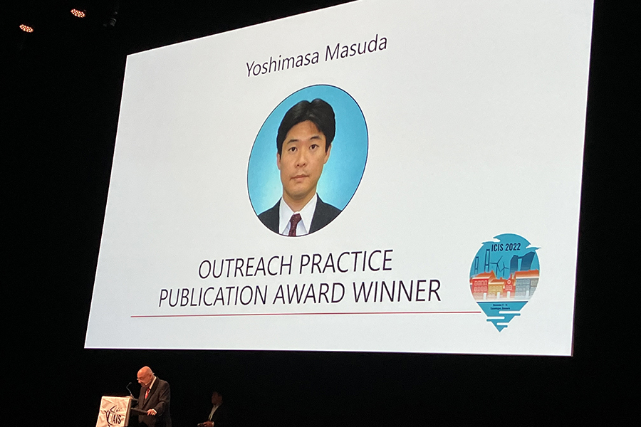 Photo of the large presentation screen at a conference. The screen shows the announcement slide for Dr. Masuda's award.