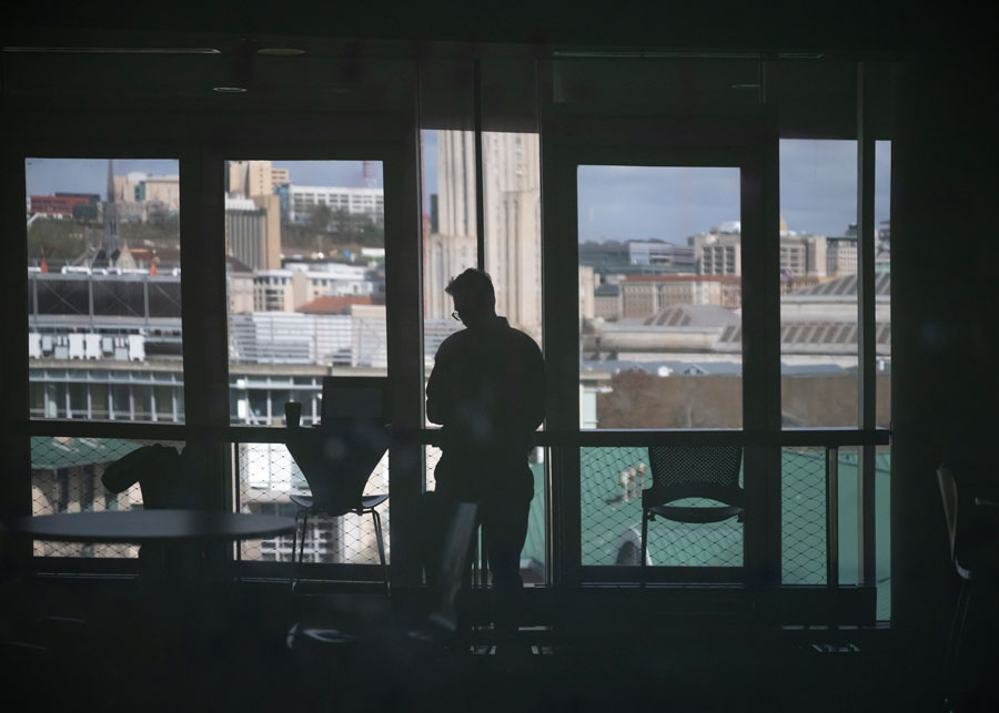 The figure of a man is silhouetted against large windows in a building.